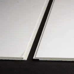 Close-up of two white gypsum ceiling tiles with different edge profiles on a black surface.