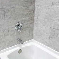 Modern bathtub with chrome faucet and lever on gray tiled walls in a clean bathroom corner.
