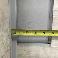 Yellow Stanley tape measure extended to 5 inches measuring grey tile spacing on a wall corner.