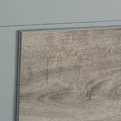 Close-up of a grayish wood floor panel with textured grain and a gray wall background.