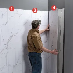 Man installing large marble-patterned wall panels in a room with gray walls and ceiling.