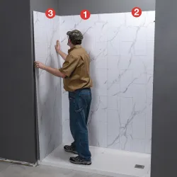 Man installing numbered large white marble pattern wall panels in a shower area against a gray wall.