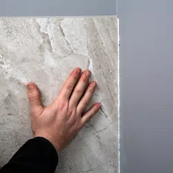 Hand pressing a large beige marble tile against a gray wall during installation or inspection process