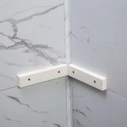 White corner bracket mounted on gray and white marble tiled walls for structural support or decoration.