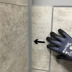 Hand wearing MaxxGrip glove aligning large gray floor tiles with arrow marking on tile.