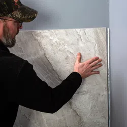 Man installing large gray marble tile on wall with adhesive in home renovation project.