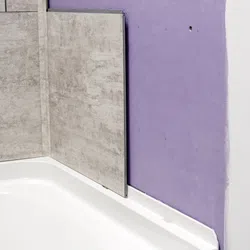 Partially installed grey wall tiles above a white bathtub next to an unfinished purple drywall corner.