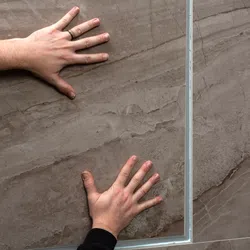 Two hands placed on large brown textured stone tiles separated by a thin silver grout line.