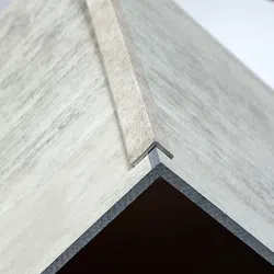 Close-up of a corner joint with a metal edge trim between two textured light gray panels forming a sharp angle.