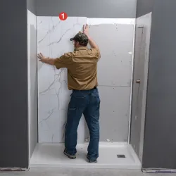 Man installing large white marble-patterned wall tiles in a shower area during renovation.