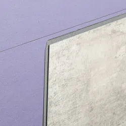 Close-up of a textured gray tile partially covering a purple fabric surface with a diagonal line.