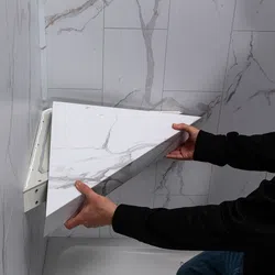 Person installing a white marble-patterned triangular shelf in a corner with marble wall tiles.
