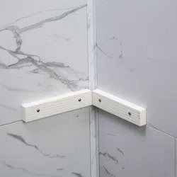 Corner of two marble patterned walls with white wooden support bars attached by screws.