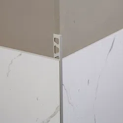 Close-up of corner edge trim installed on marble-patterned wall tiles with light gray painted wall above.
