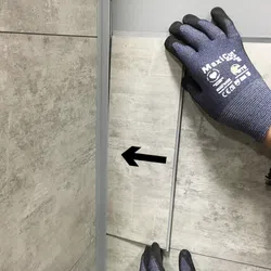 Hand wearing protective gloves installing or aligning rectangular stone tile with black arrow on wall