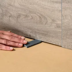 Hand placing a leveling spacer under wood grain floor panels during flooring installation for alignment.
