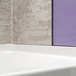 Close-up of a white bathtub with textured gray and purple bathroom wall tiles behind it.