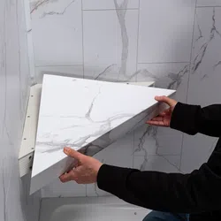 Person installing a removable white marble patterned corner panel in a tiled bathroom corner.