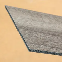 Close-up of a gray wood-textured vinyl plank with a beveled edge against a beige background