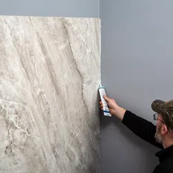 Man applying adhesive to install large marble slab on gray wall in home interior renovation.