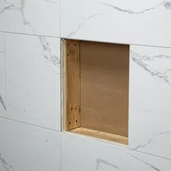 White marble tiled wall with a square cutout revealing wooden framing behind the tile surface.