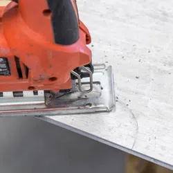 Close-up of a red jigsaw cutting a curved line into a white tile on a workbench with tile dust.
