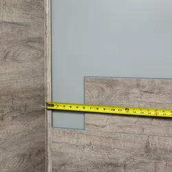 Worker measuring wood paneling with a yellow tape measure against a gray wall during installation.