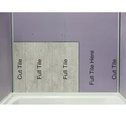 Wall with labeled areas for cut and full tiles partially installed above a bathtub in a bathroom.