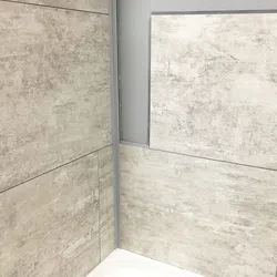 Close-up of beige textured wall tiles in a corner above a white bathtub with gray grout lines.