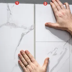 Two hands aligning white marble tiles with gray veining during floor installation close-up.