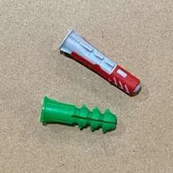Two different colored plastic wall anchors, one green and one gray with red, on a beige surface.