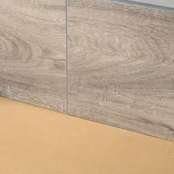 Close-up of two light brown wood-textured tiles placed on a beige surface with clear grout lines.