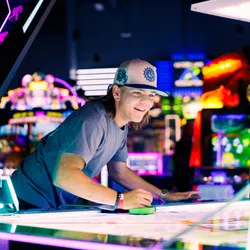 Young man playing air hockey at brightly lit arcade with colorful game machines in the background