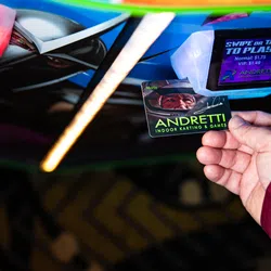 Hand holding an Andretti Indoor Karting & Games swipe card near a ticket scanner with pricing displayed.