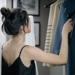 a woman in a black tank top looking at sweater hanging in a closet