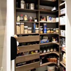 Organized kitchen pantry with shelves and jars filled with cereals, spices, and canned goods in a modern home.