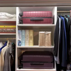 Organized closet with hanging jackets, folded shirts, two suitcases, board games, and storage boxes on shelves.