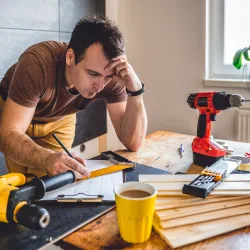 Man working on installing a DIY closet with electric drill, drill bits and wooden pieces on a table