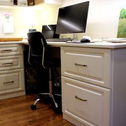 Modern home office setup with white cabinets, wooden floor, black swivel chair, and large computer monitor.
