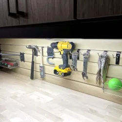 Organized workshop wall with tools including drill, hammer, wrench, pliers, and green balls under dark cabinets.