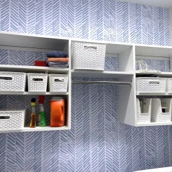 White wicker baskets organized on wall-mounted shelves with patterned blue wallpaper in laundry room