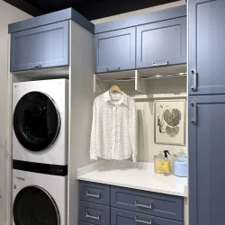 Modern laundry room with stacked washer and dryer, blue cabinetry, white countertop, and hanging clothes