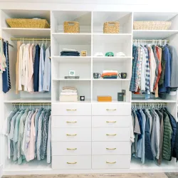 Organized white walk-in closet with hanging clothes, folded items, shoes, drawers, and woven baskets.