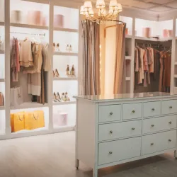 Organized walk-in closet with clothing racks, shoes, handbags, a white island dresser, and chandelier lighting.