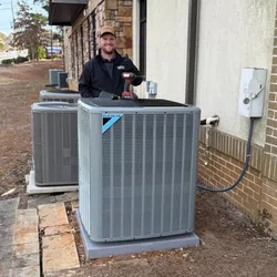 Technician standing next to Daikin HVAC units installed outside a brick and stone building on a construction site.