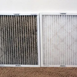 Two air filters side by side showing a dirty dark filter on left and a clean white filter on right on carpeted floor.