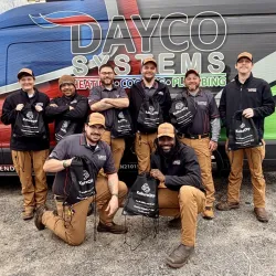 Dayco Systems team of technicians posing in front of a branded van with tools and bags, wearing uniforms and caps.