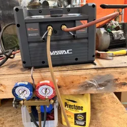 WAVAC vacuum pump connected to refrigeration gauges on a wooden workbench with tools and coolant container.