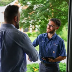 Service technician shaking hands with homeowner at front door during a home visit in a green neighborhood.
