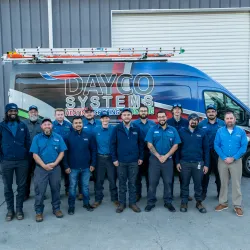 Team of Dayco Systems HVAC technicians standing in front of a branded service van at a warehouse.